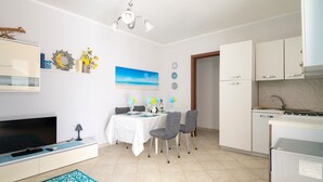 Une cuisine moderne avec des meubles blancs, une table à manger avec des chaises, un téléviseur à écran plat et un luminaire au plafond.