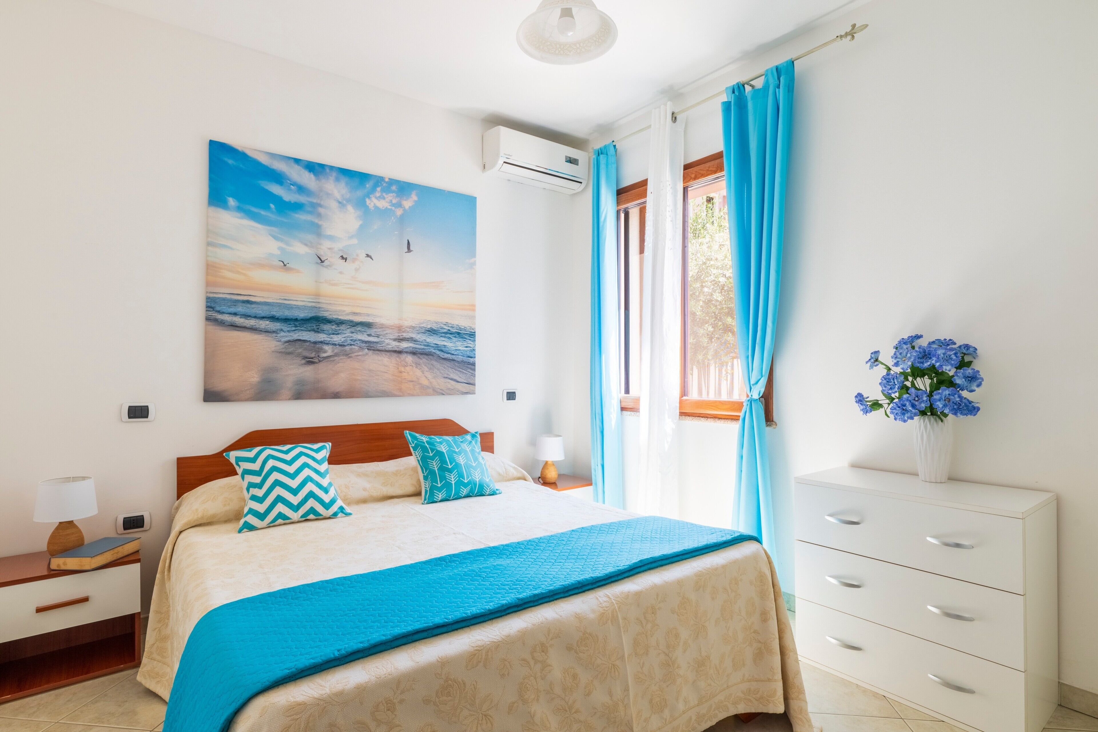 Un dormitorio con cama, mesita de noche, cómoda, ventana con cortinas y aire acondicionado de pared.