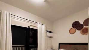 Una habitación de hotel con cama, ventana con cortinas, aire acondicionado y una pared decorada con placas.