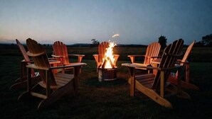 Quatre fauteuils Adirondack en bois disposés autour d’un foyer métallique où brûlent des flammes.
