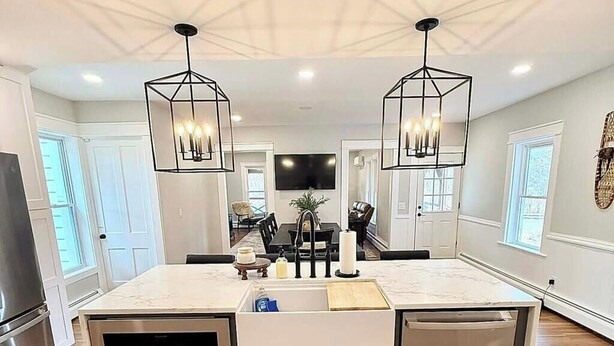 Une cuisine moderne dotée d’un îlot central, de luminaires suspendus et donnant sur l’espace repas.