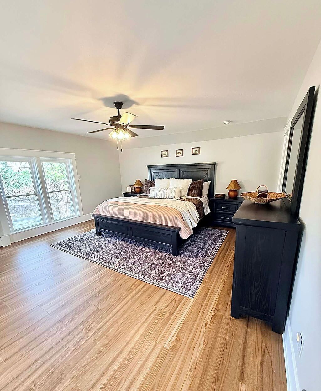 A bedroom with a bed, a ceiling fan, a dresser, and a large window.