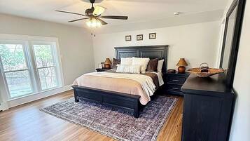 A bedroom with a bed, a ceiling fan, a dresser, and a large window.