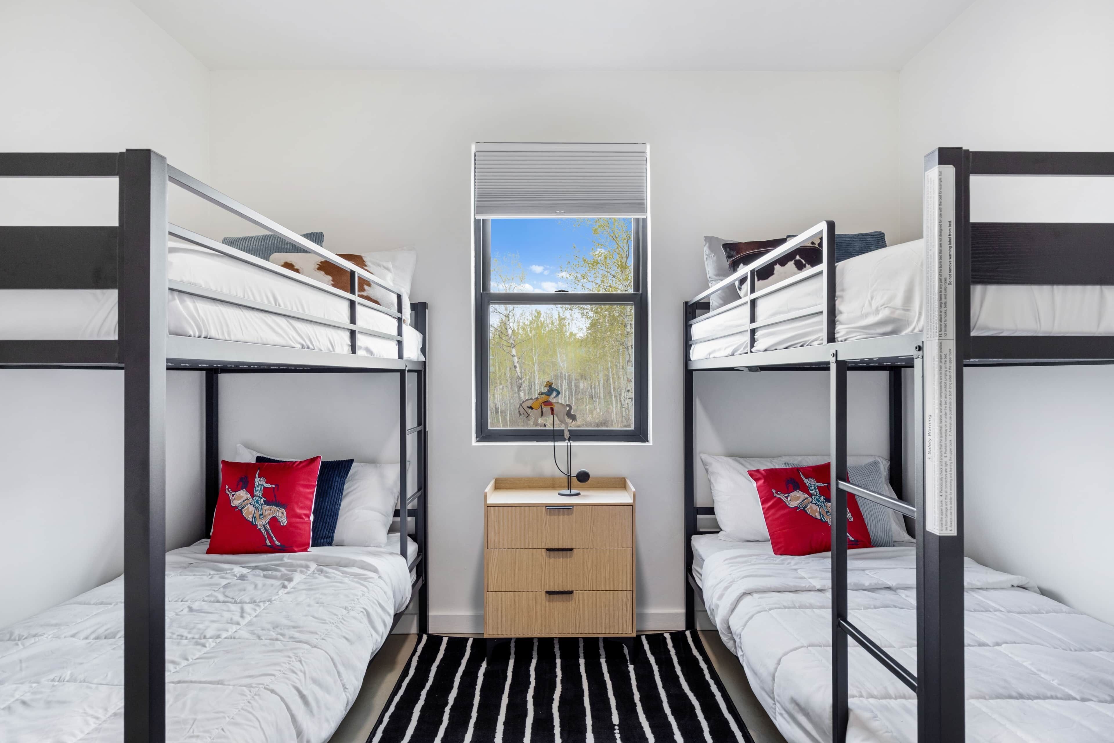 A bunk bed room with a window, a bedside table, and a striped rug.