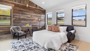 Un dormitorio con una cama grande, un panel de madera decorativo, una silla, una mesita y una ventana.