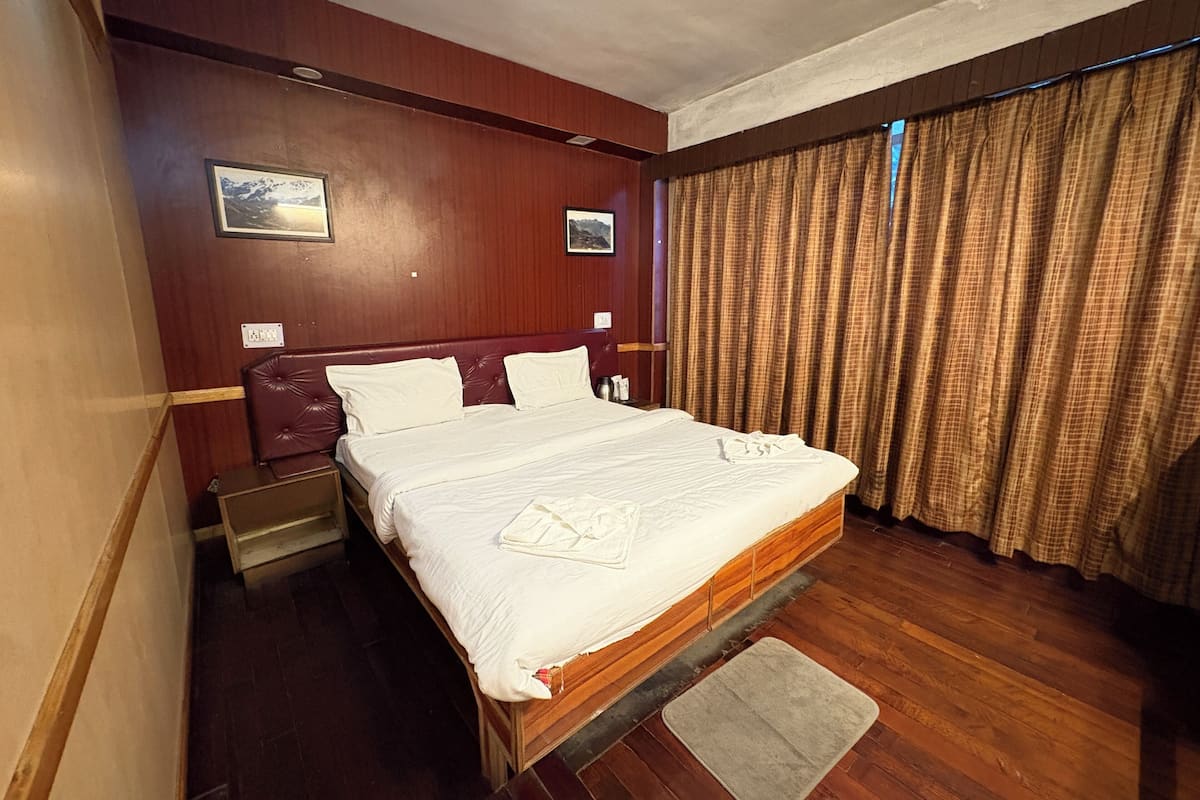 Ein Hotelzimmer mit einem hölzernen Bett, einem Nachttisch, Vorhängen vor dem Fenster und einem an der Wand hängenden Bild.