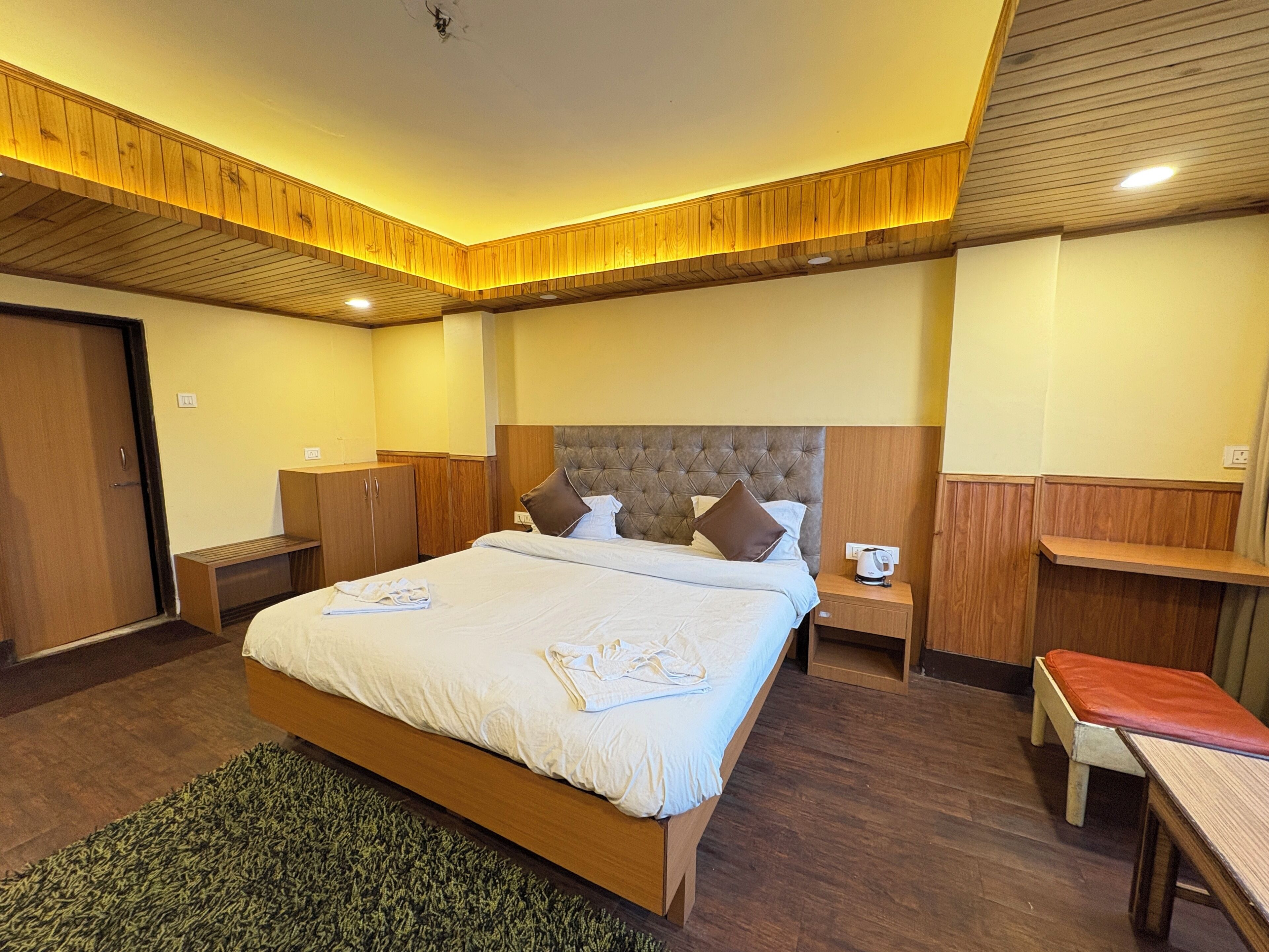 Ein Hotelzimmer mit einem großen Bett, einem Holzkopfende, Nachttischen, einer Bank und einem Kleiderschrank.