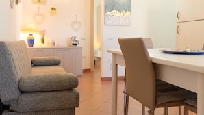 Un salon avec un canapé, une table à manger et des chaises, un coin cuisine et une porte donnant sur une autre pièce.