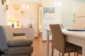 A living room with a sofa, a dining table with chairs, a kitchen area, and a door leading to another room. - Villa Ludovica - Two Bedroom Apartment, Sleeps 4 (Tanaunella)