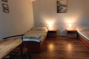 Eine kleine, einfache Unterkunft mit zwei Betten, einem Holztisch und Nachttischlampen.