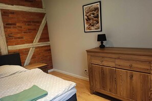 Quarto com cama, penteadeira de madeira, mesa de cabeceira, abajur e quadro na parede.