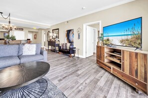 Een woonkamer met een bank, salontafel, tv-meubel en een eethoek met stoelen en een tafel.