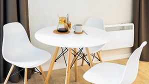 Una pequeña mesa redonda con una cafetera y una taza, flanqueada por dos sillas blancas.