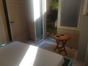 A room with a bed, a small wooden stool, a sliding glass door leading to a garden, and a window with blinds. - Lake 0 Central Lugano Family Apartment Lake View (7 guests) (LUGANO)
