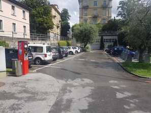 A parking lot with several cars, a parking meter, and buildings in the background. - Lugano Deluxe 2 bedroom lake view (6 guests) (LUGANO)
