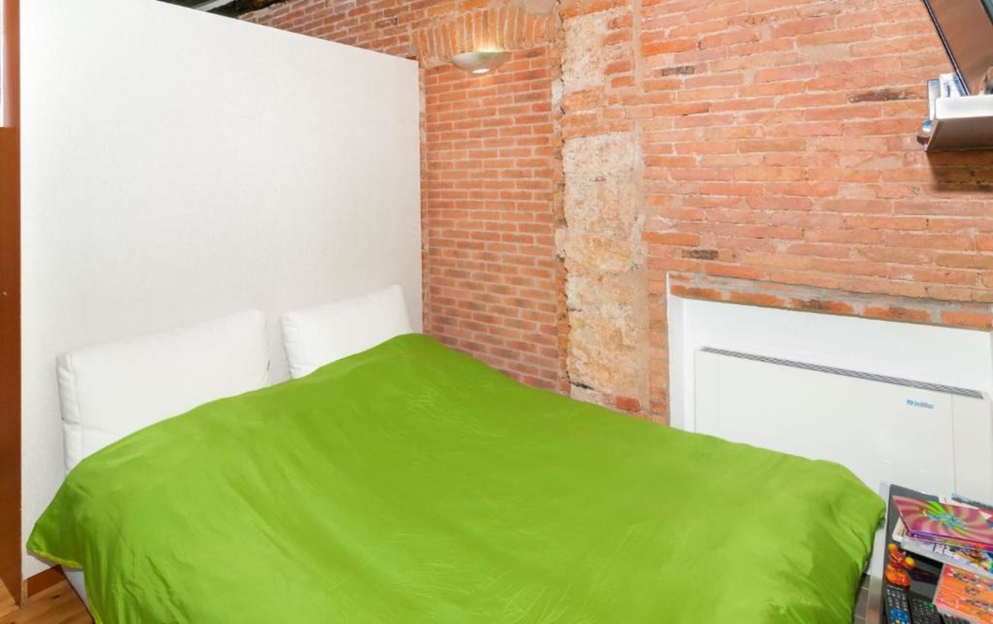 Ein Zimmer mit Backsteinwand, einem weißen Bett mit grüner Bettdecke und einem weißen Kleiderschrank.
