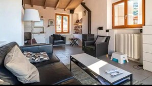 A living room with a sofa, coffee table, and a fireplace. There is a kitchen area with a stove and a radiator. - Cadro Casa Vista (4guests) (SESTRI LEVANTE)