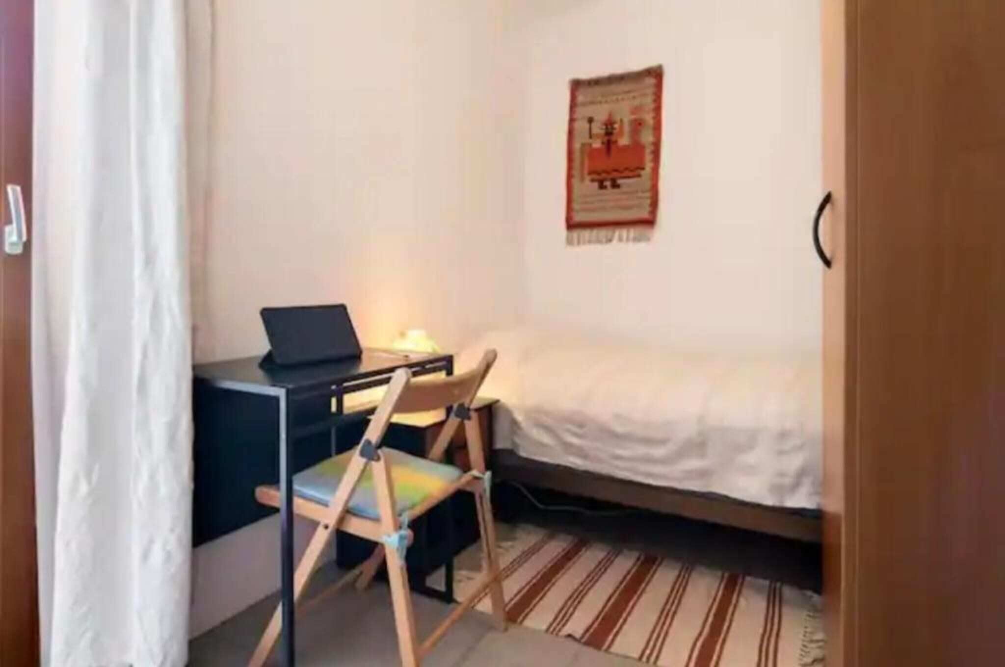 Ett sovrum med en säng, ett skrivbord med en bärbar dator, en stol och en affisch som hänger på väggen.