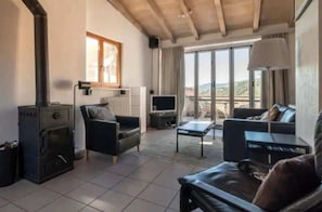 Ein Wohnzimmer mit Kamin, einer Couch, einem Fernseher und Blick ins Freie.