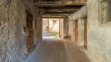 Un estrecho pasillo con paredes de piedra tosca, puertas de madera y una escalera que sube a un nivel superior.