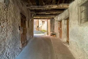 Ein schmaler Gang mit rauen Steinwänden, Holztüren und einer Treppe, die in eine obere Ebene führt.