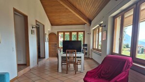 A room with a tiled floor, wooden ceiling, a television, a table with chairs, and a covered chair. - PREGASSONA Executive Apartment Lake View and Garden (8persons) (Lugano Pregassona)