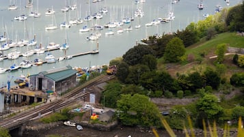 A marina with numerous boats docked, a parking area with cars, and a hilly landscape in the background.