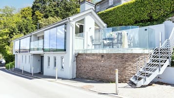 Una casa moderna con un balcón de vidrio, un muro de ladrillo y una escalera que lleva al piso superior.
