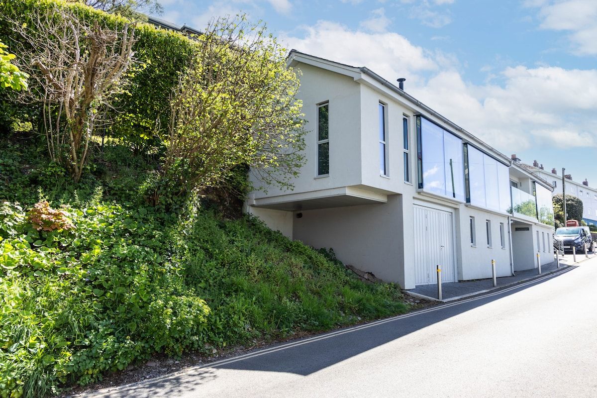 A modern two-story residential building with a garage, situated on a street with a clear sky.
