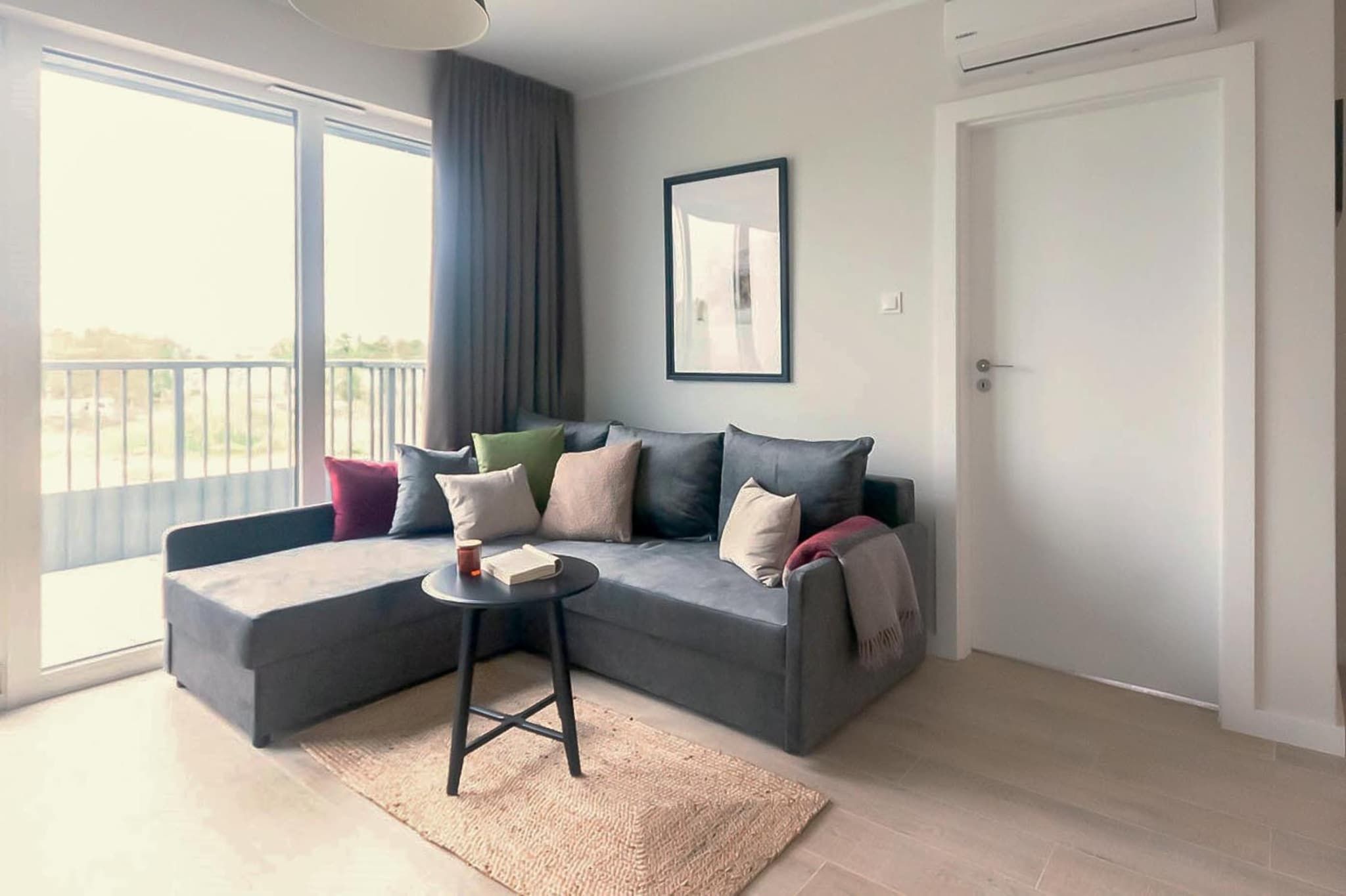Una sala de estar moderna con un sofá seccional gris, una mesita redonda y un ventanal con vistas.