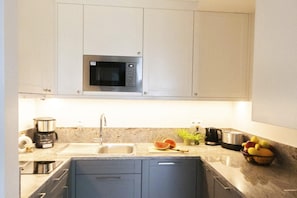 A modern kitchen with a built-in microwave, stainless steel appliances, a sink, and a countertop with fruits and a coffee maker.