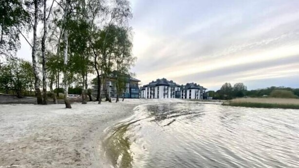 A waterfront hotel with a sandy beach, trees, and a calm river.