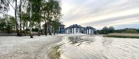 A riverside hotel with a sandy beach and trees.
