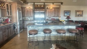 A spacious kitchen with a central island, bar stools, and a dining area with chairs. - Lake Roosevelt Retreat - Spring Canyon Boat Launch (Grand Coulee)