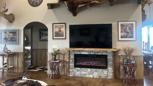 A living room with a stone fireplace, mounted television, and deer antlers on the wall. - Lake Roosevelt Retreat - Spring Canyon Boat Launch (Grand Coulee)