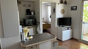 A compact kitchen with a microwave, toaster, and a small refrigerator. There is a dining area with a table and chairs, and a TV on a stand. - Air-conditioned apartment for 4 near town center. Small dogs accepted (La Londe-les-Maures)