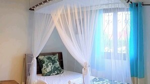 Una cama individual con dosel, una mesita de noche con un radio y una ventana con cortinas.