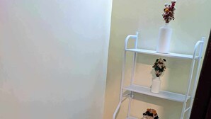 Un baño pequeño con inodoro de madera, un estante blanco con un florero y un dispensador de papel higiénico.