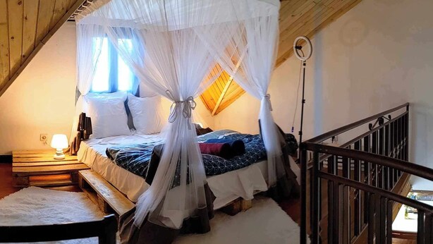 Un dormitorio con cama de dosel, cabecera de madera, mesita de noche con lámpara y una silla.