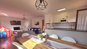 A modern dining area with a wooden table, white chairs, and a kitchen in the background. - 20807 Casa Mira Mijedo - House in Argoños (Argoños)