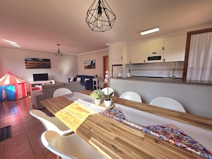 Un comedor moderno con una mesa de madera, sillas blancas y una cocina al fondo.