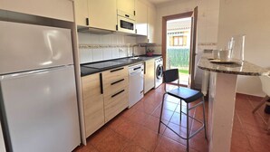 A compact kitchen with a refrigerator, oven, microwave, dishwasher, and a small dining area with a chair. - 20807 Casa Mira Mijedo - House in Argoños (Argoños)