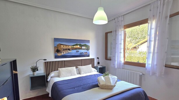 A bedroom with a bed, a nightstand, a lamp, a painting, a window with curtains, and a radiator. - 20807 Casa Mira Mijedo - House in Argoños (Argoños)
