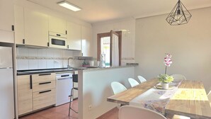 A kitchen with white cabinets, a microwave, and a dishwasher. There is a dining table with chairs and a hanging light fixture. - 20807 Casa Mira Mijedo - House in Argoños (Argoños)