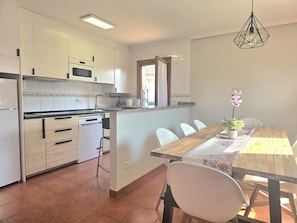 Una cocina con armarios blancos, microondas y lavavajillas. Hay una mesa de comedor con sillas y una lámpara colgante.