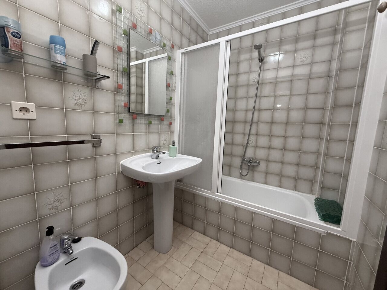 A bathroom with a sink, mirror, shower, and tiled walls.