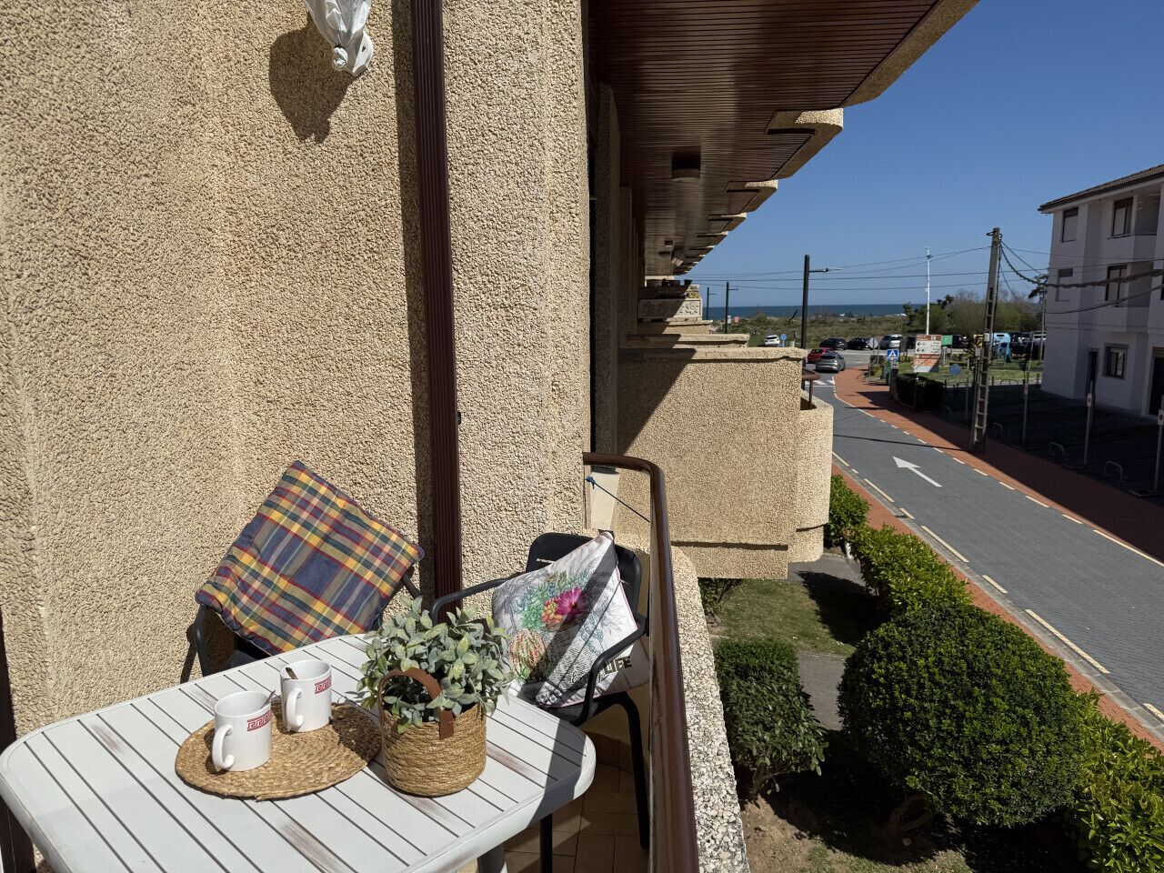 A balcony with a table, chairs, and a view of a street.