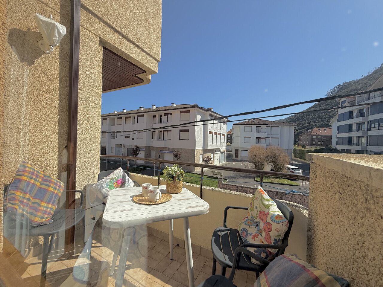 A balcony with a table and chairs, a view of buildings, and a clear sky.