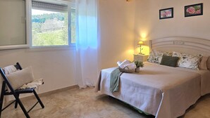 A bedroom with a bed, a chair, a window with curtains, a bedside table with a lamp, and two framed pictures on the wall. - La Encina de Güemes - 13008 (Güemes)