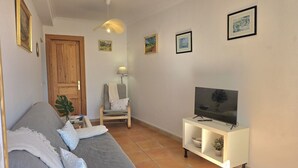 A living room with a sofa, a TV on a stand, a chair, and a door. - La Encina de Güemes - 13008 (Güemes)